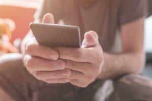 Man using mobile phone at home, close up of male hands addicted to smartphone, selective focus