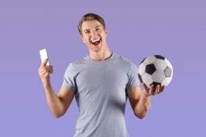 Young football fan watching championship online on smartphone, happy over victory of his team on lilac background