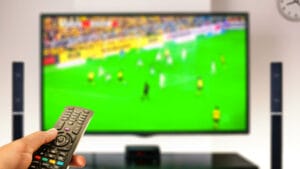 watching soccer at home tv with remote control on hand